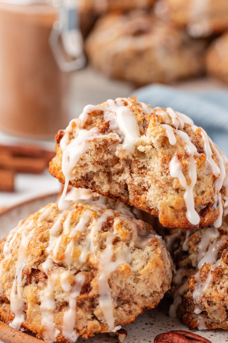 cinnamon bun scones piled on a plate with a bite missing from the top scone
