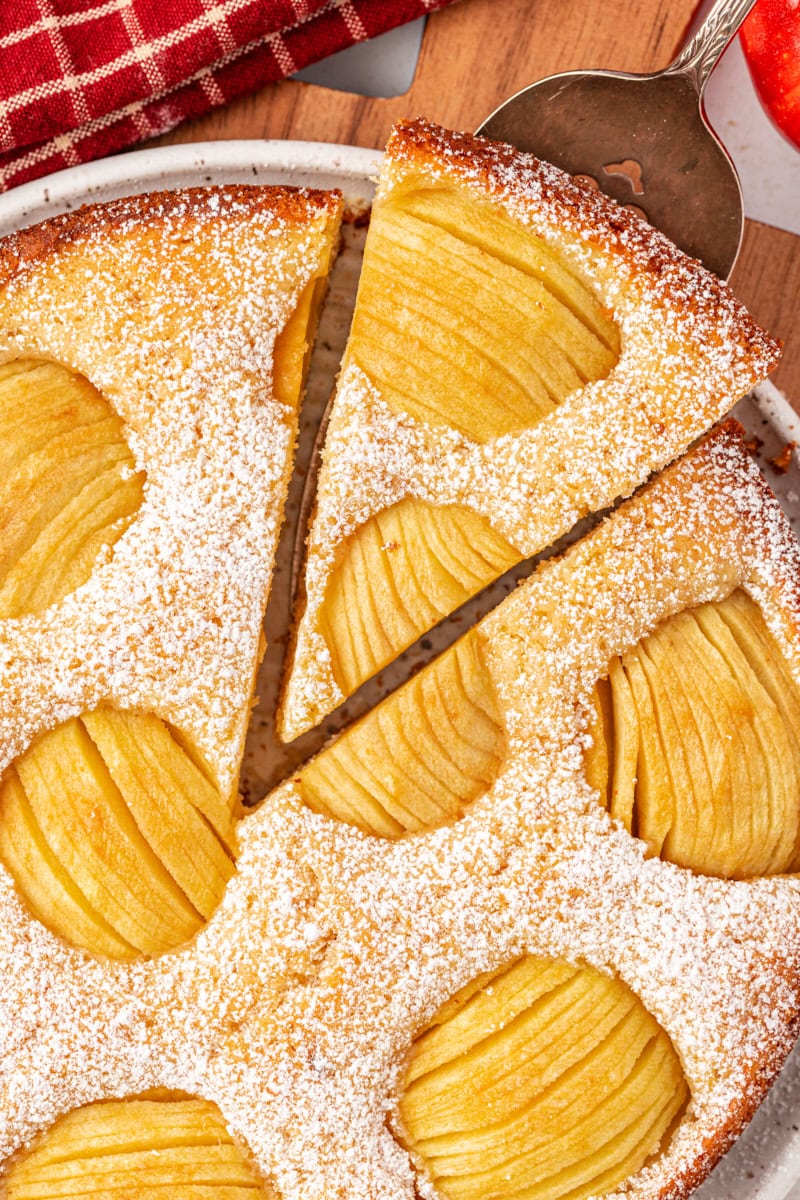 overhead view of a slice of German apple cake on a cake server being removed from the remaining cake