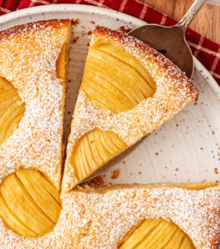overhead view of partially sliced German apple cake topped with fanned apple slices and dusted with powdered sugar
