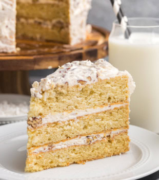 a slice of Italian cream cake on a white plate with the remaining cake in the background