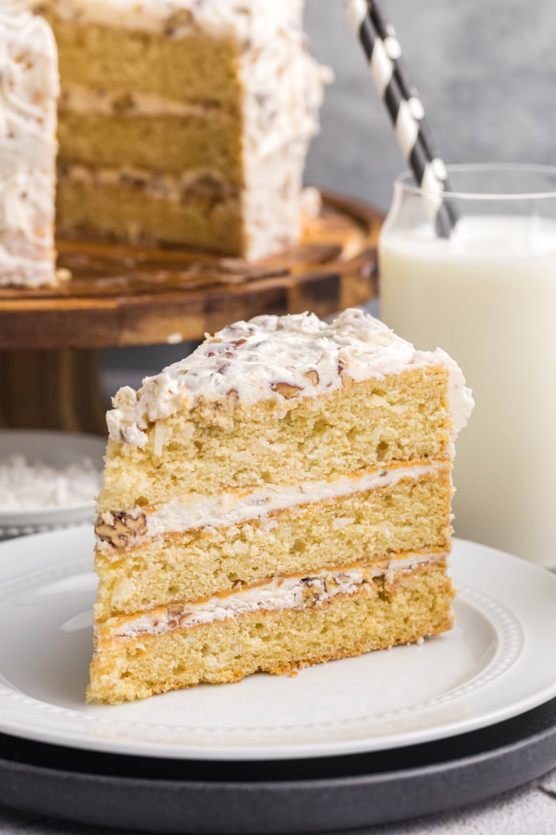 a slice of Italian cream cake on a white plate with the remaining cake in the background