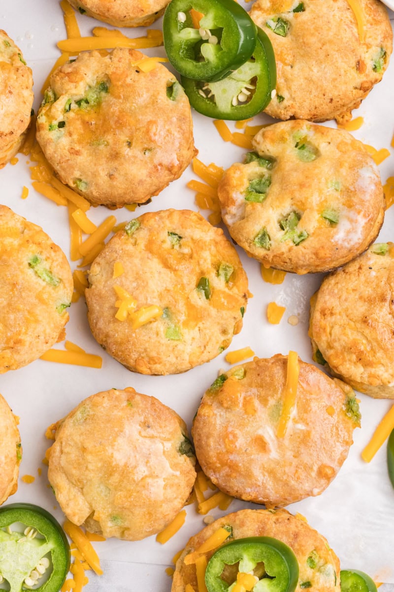overhead view of jalapeño cheddar biscuits on a white surface with more cheese and peppers scattered around them