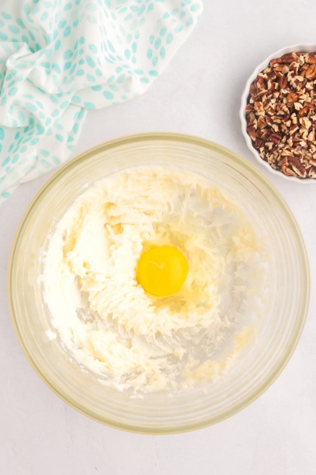 overhead view of egg added to creamed butter, cream cheese, and sugar in a glass mixing bowl