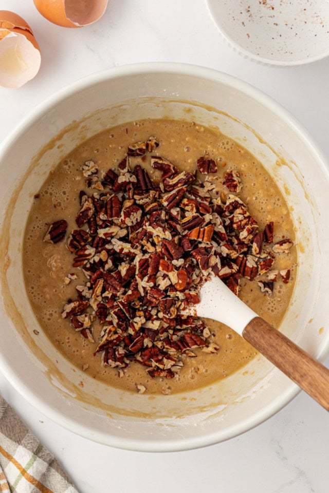 overhead view of chopped toasted pecans added to pecan praline muffin batter in a white mixing bowl