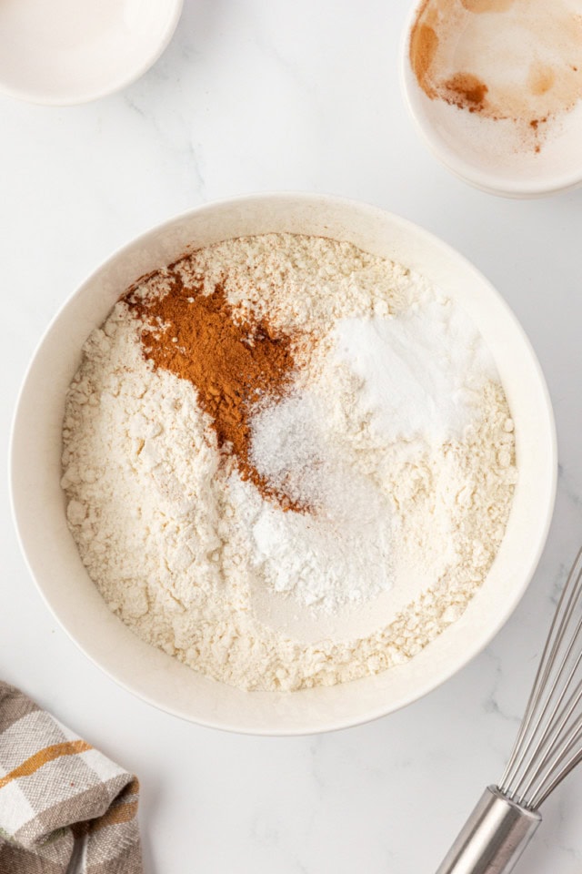 overhead view of flour, baking powder, baking soda, salt, and cinnamon in a white mixing bowl