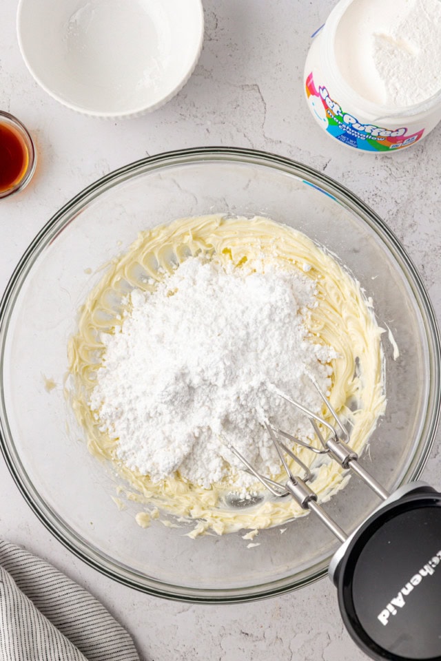 overhead view of confectioners' sugar added to creamed butter in a glass mixing bowl