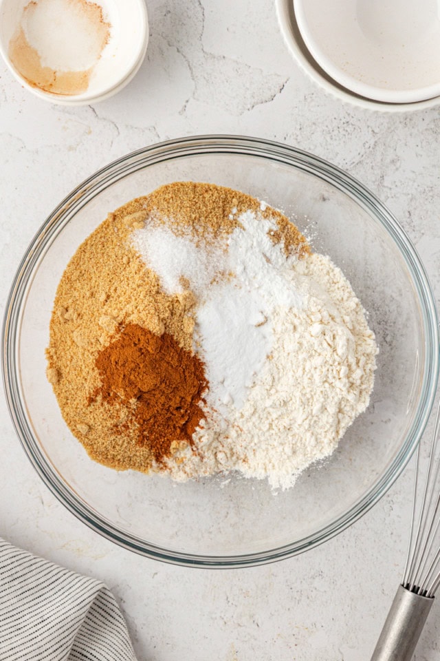 overhead view of flour, graham cracker crumbs, baking soda, baking powder, cinnamon, and salt in a glass mixing bowl