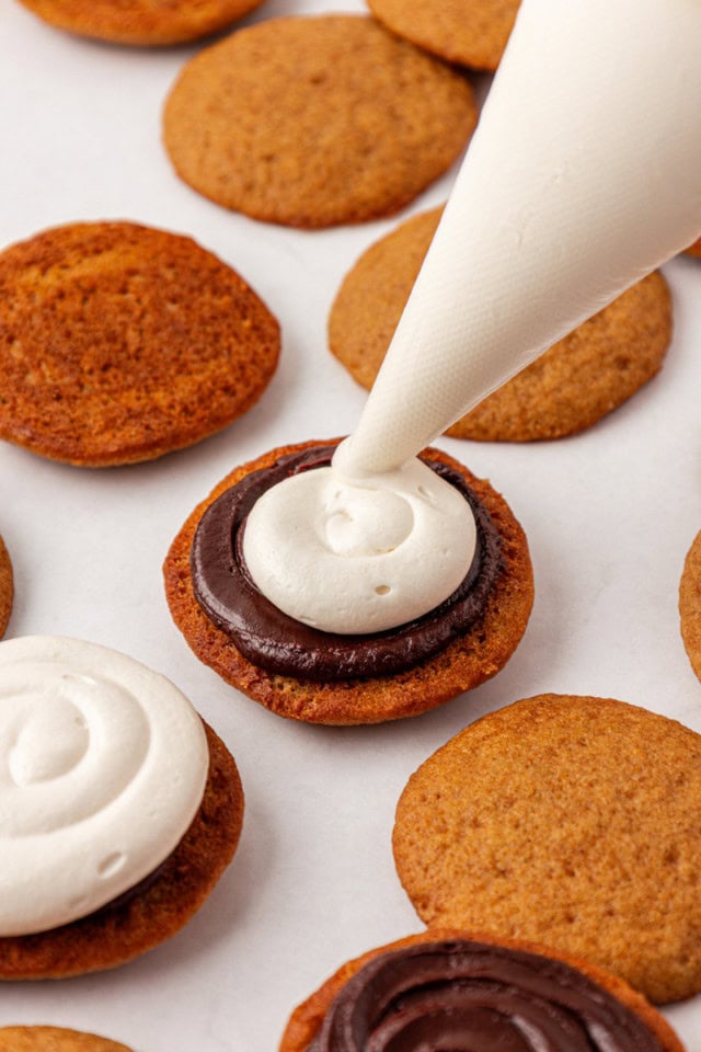marshmallow buttercream being piped onto chocolate ganache spread on the bottom of a graham cake