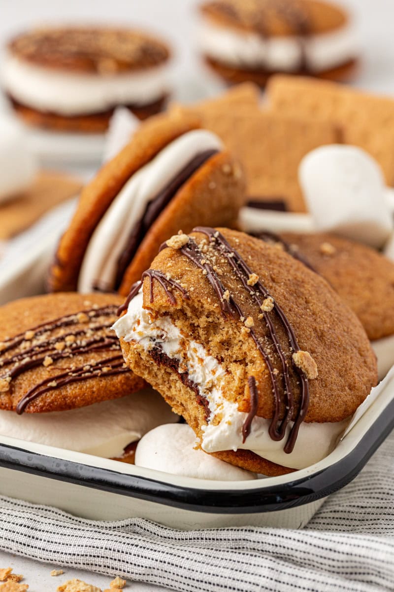 s'mores whoopie pies in a black-rimmed white tray with a bite missing from the front whoopie pie