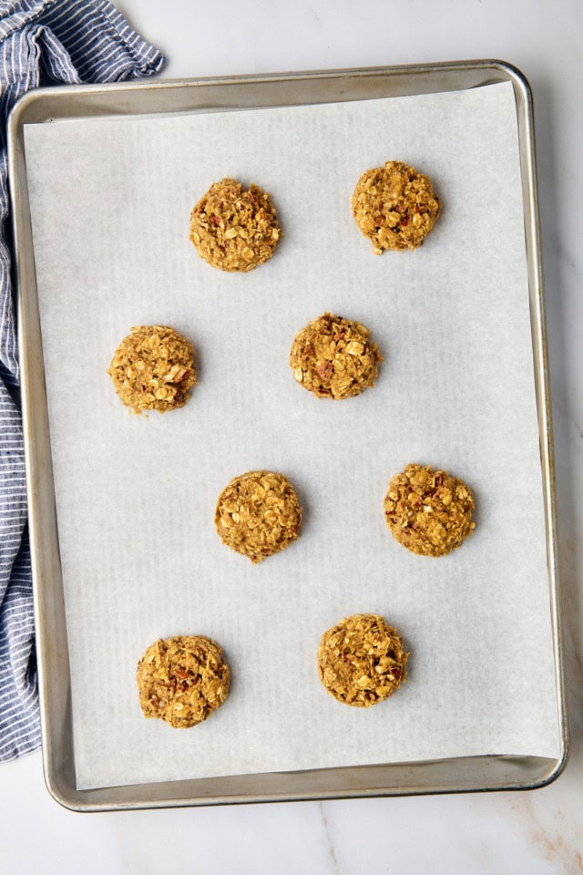 overhead view of flattened brown butter maple oatmeal cookies on a parchment-lined baking sheet ready to go into the oven