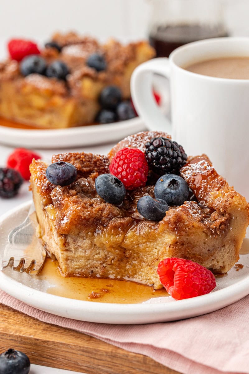 a slice of baked French toast topped with maple syrup and fresh berries on a white plate