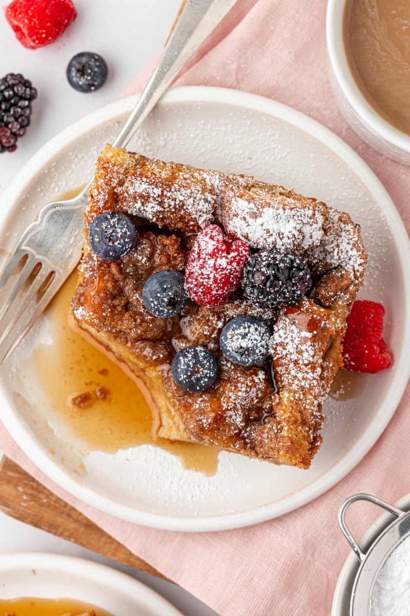 overhead view of a slice of baked French toast on a white plate with a bite missing
