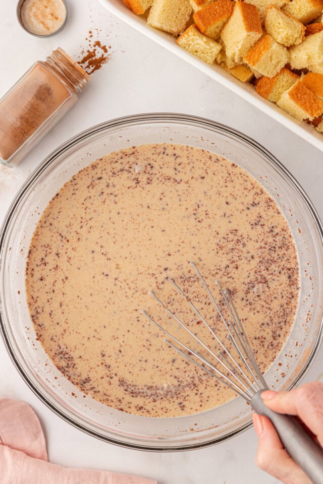 overhead view of eggs, milk, cream, sugar, vanilla, and spices whisked together in a glass bowl