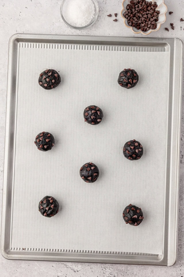 overhead view of black cocoa cookie dough scooped onto a lined baking sheet, ready to go into the oven
