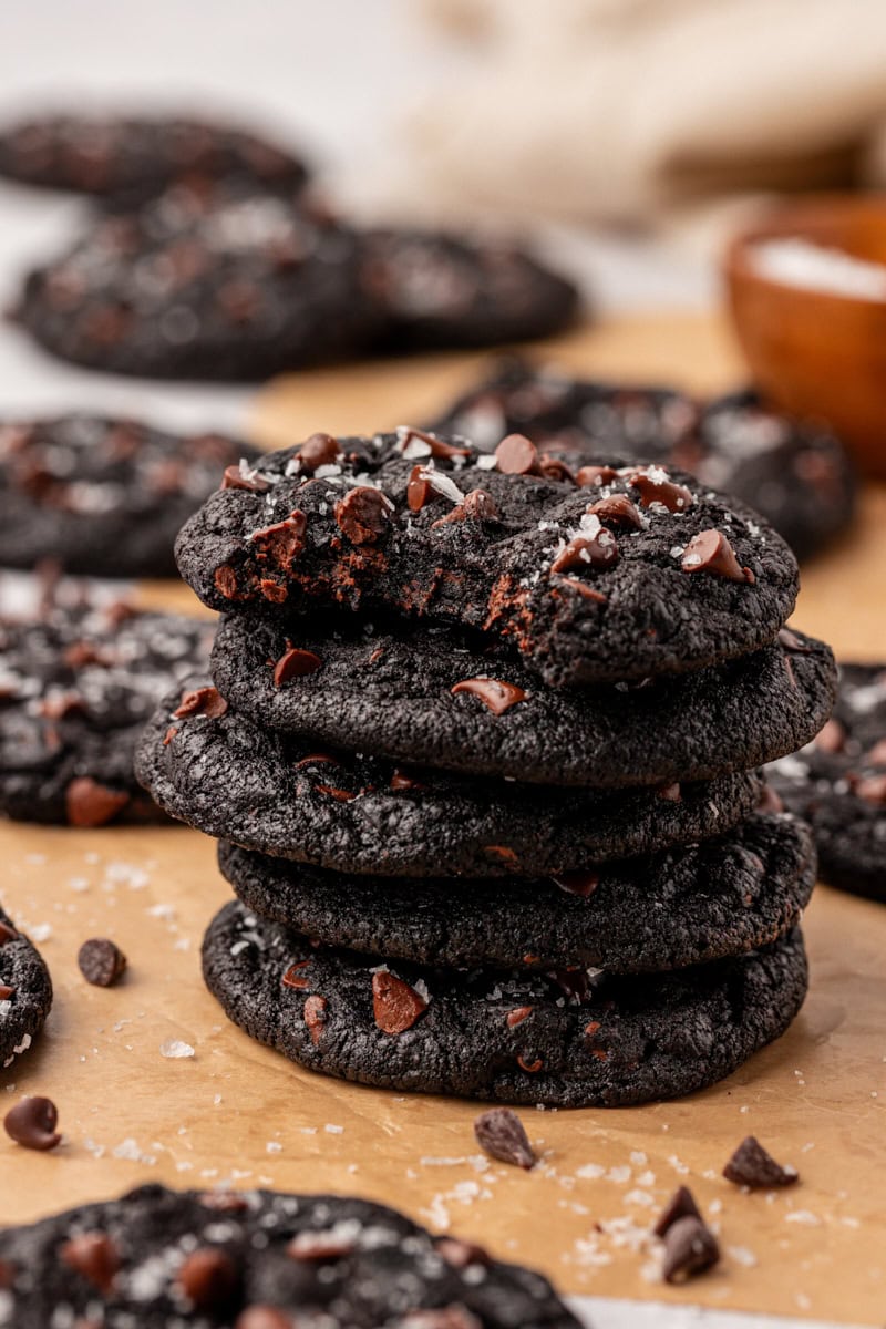 stack of five black cocoa cookies on parchment paper with a bite missing from the top cookie