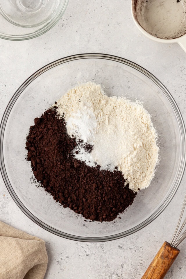 overhead view of flour, black cocoa powder, baking soda, and salt in a glass mixing bowl