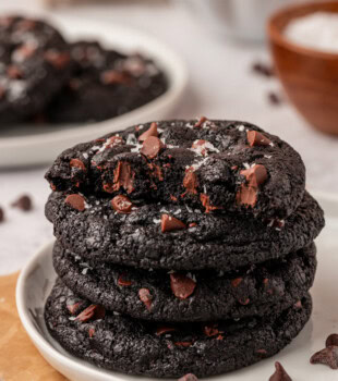 stack of four black cocoa cookies on a white plate with more cookies in the background