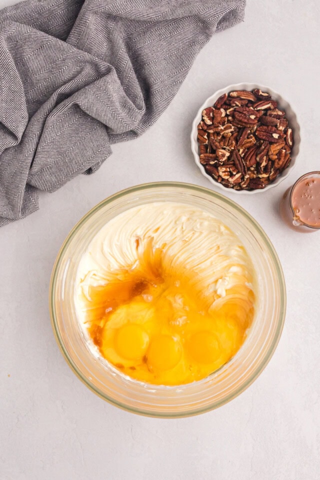 overhead view of eggs, bourbon, and vanilla added to beaten cream cheese and sugar in a glass mixing bowl