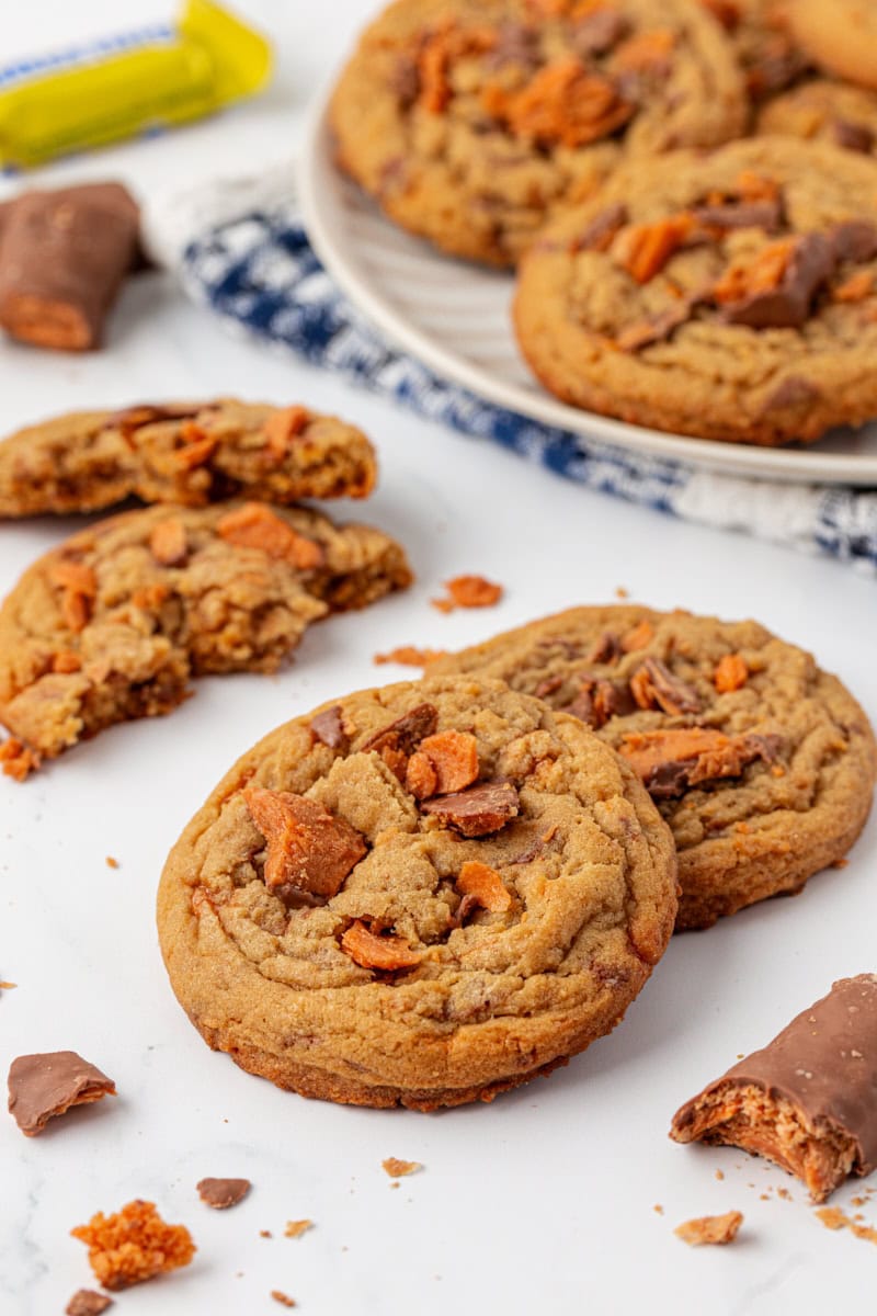 two Butterfinger cookies on a white surface with more cookies in the background