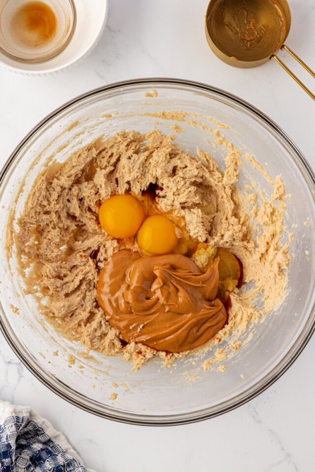overhead view of peanut butter, eggs, and vanilla added to creamed butter and sugars in a glass mixing bowl