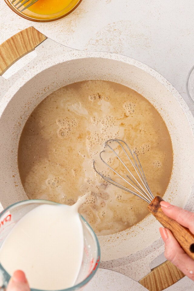 overhead view of milk being whisked into melted butter and brown sugar in a white saucepan