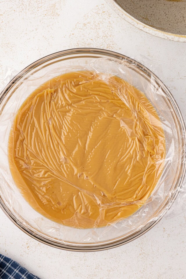 overhead view of butterscotch pie filling covered with plastic wrap in a glass bowl