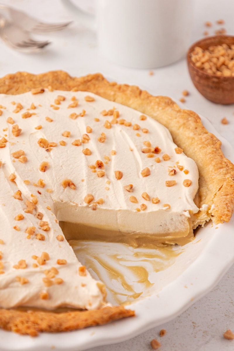 butterscotch pie topped with brown sugar whipped cream in a white pie plate with two slices missing