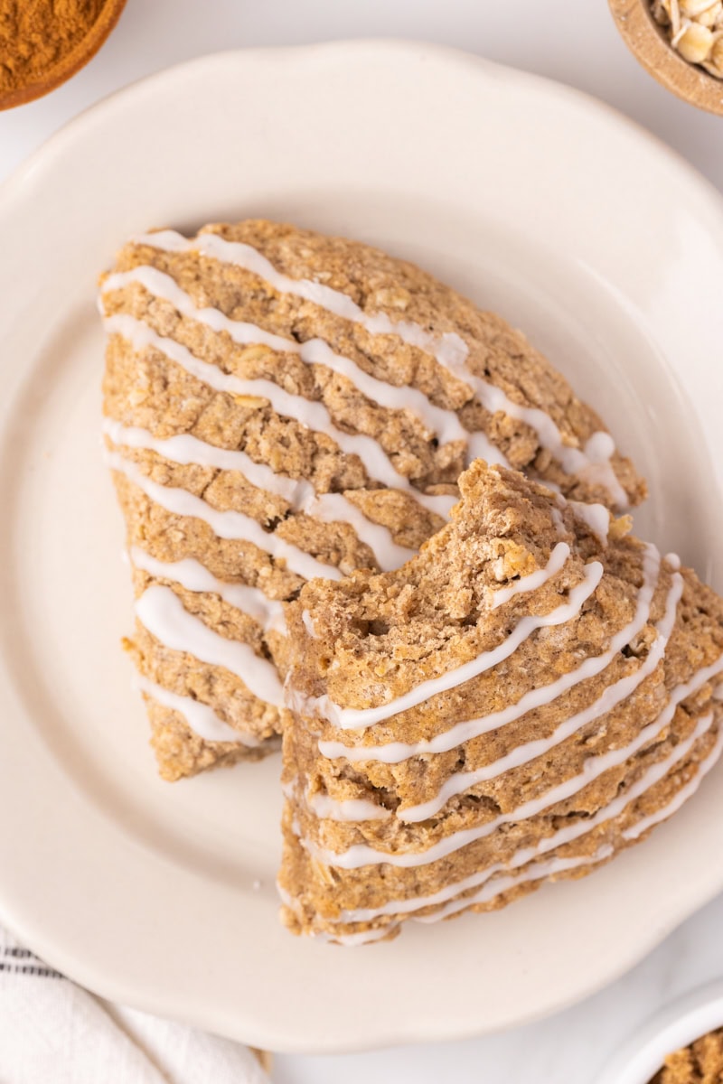 two cinnamon oat scones on a white plate with a bite missing from one of the scones