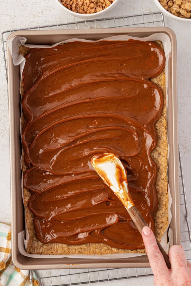 overhead view of heated dulce de leche being spread over partially baked oat crust