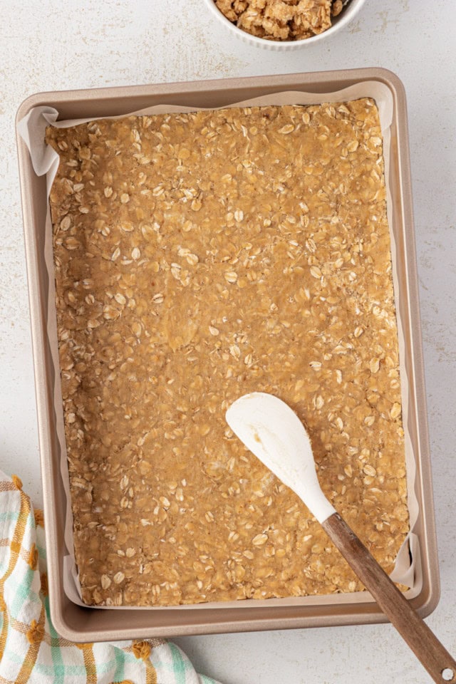 overhead view of oat crust mixture pressed into the bottom of a lined 9x13 pan