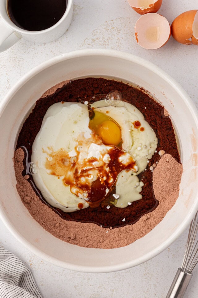 overhead view of eggs, oil, vanilla, and buttermilk added to dry ingredients for chocolate cake
