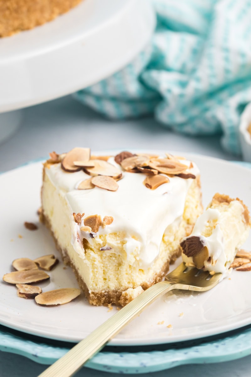 a creamy slice of amaretto cheesecake topped with a glossy sour cream layer and toasted almonds, with a forkful showing the smooth, rich texture