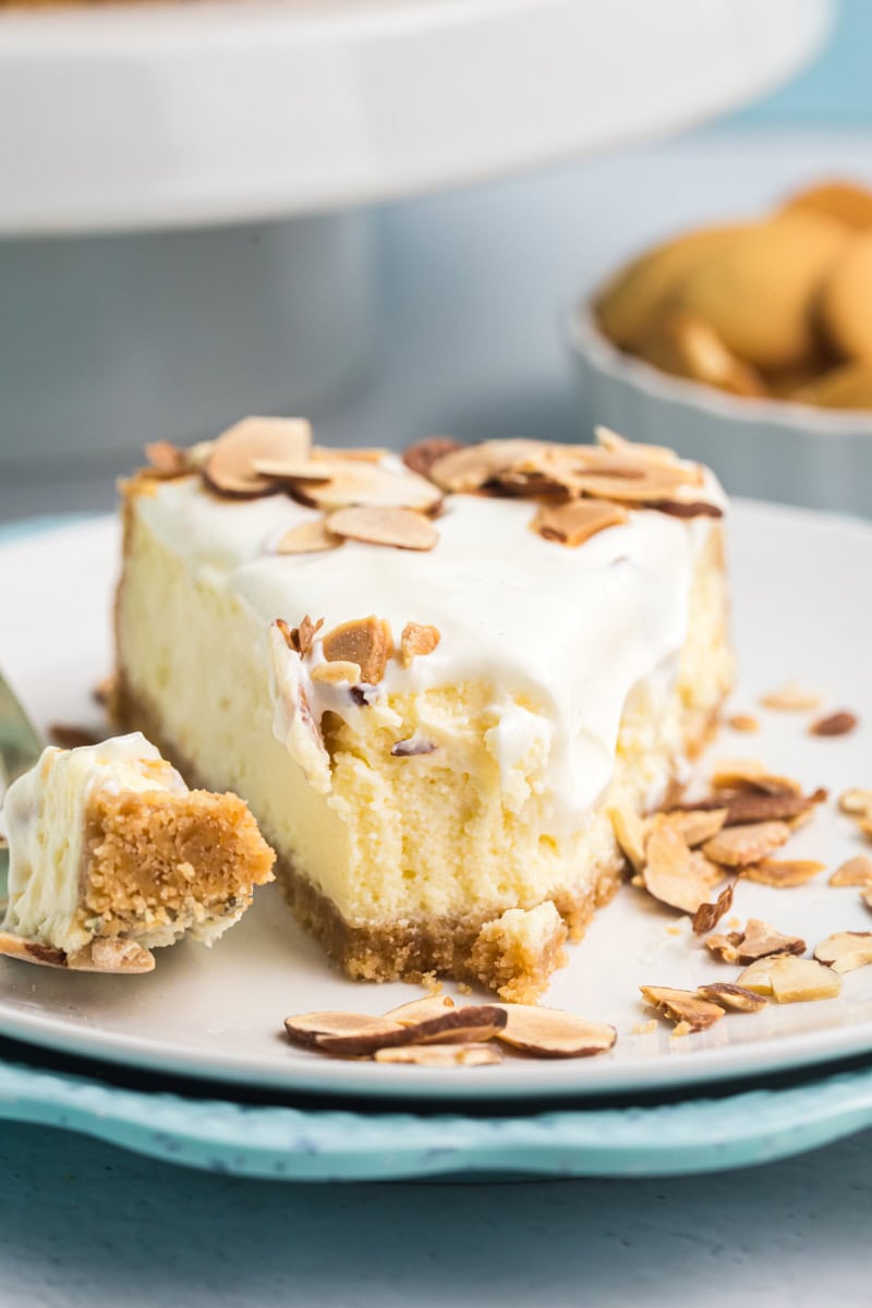 a slice of amaretto cheesecake on a white plate, topped with toasted almonds and a creamy sour cream layer, showing its rich texture and golden crust