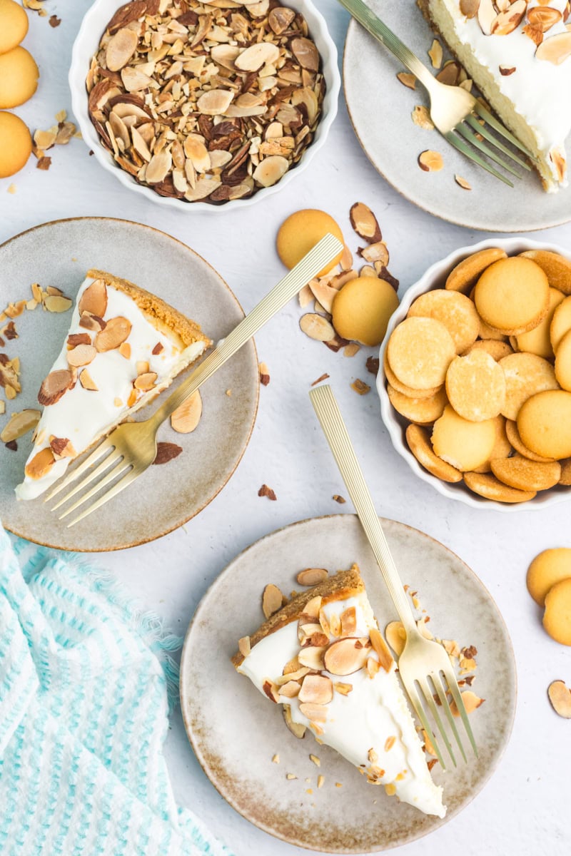 overhead view of two slices of amaretto cheesecake on plates, surrounded by toasted almonds and vanilla wafers