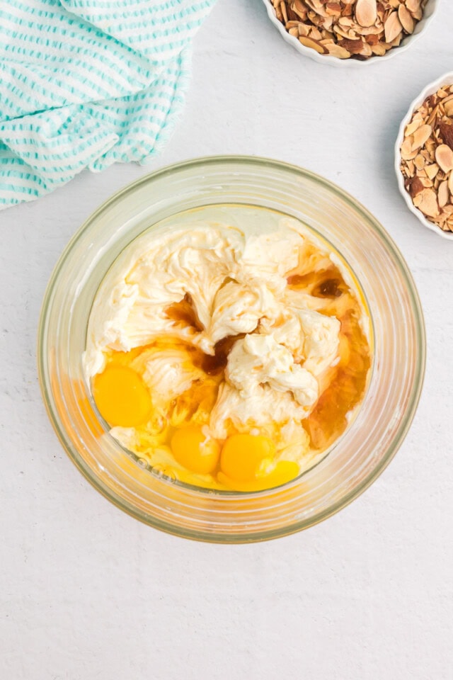 overhead view of eggs, amaretto, and extracts added to beaten cream cheese and sugar