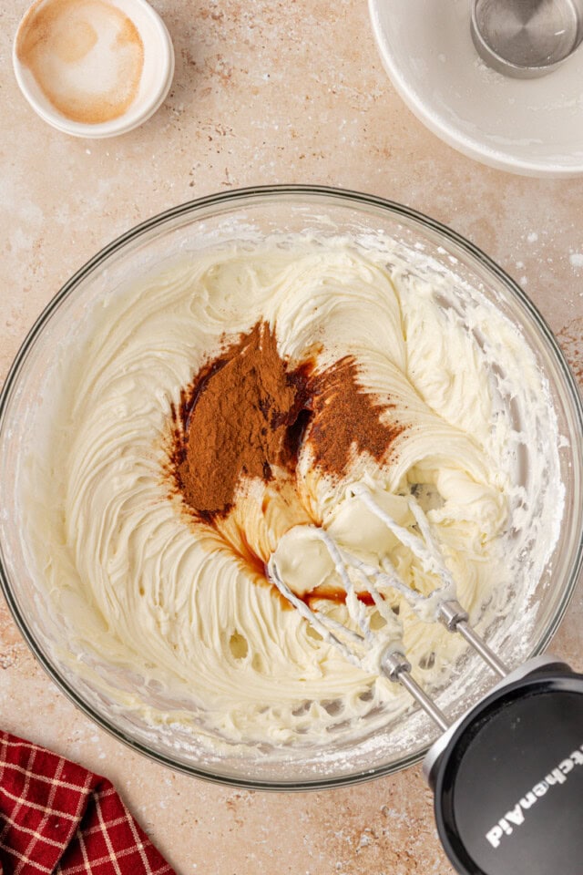 overhead view of vanilla, cinnamon, and nutmeg added to cream cheese frosting mixture