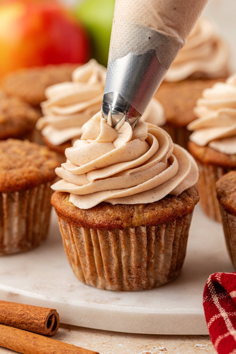 spiced cream cheese frosting being piped onto an apple cupcake, with more cupcakes in the background