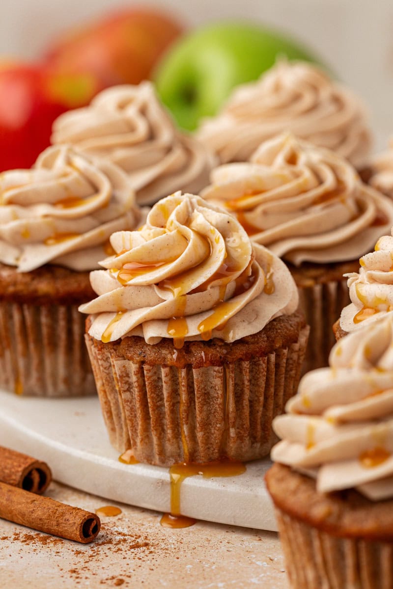 apple cupcakes topped with spiced cream cheese frosting and caramel on a marble serving tray