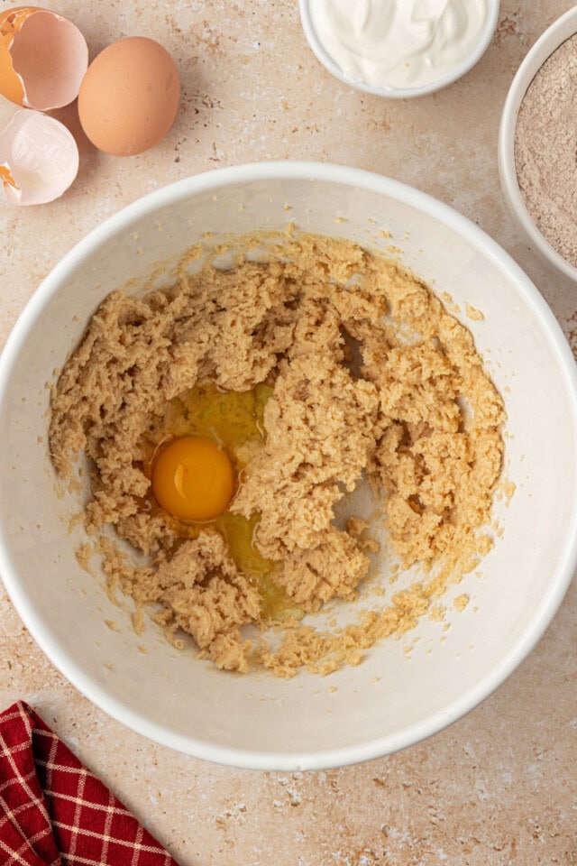 overhead view of egg added to creamed butter and sugar in a white mixing bowl