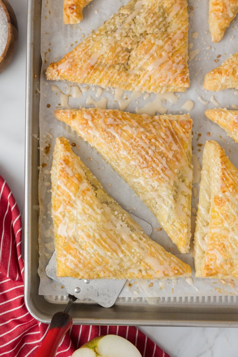 overhead view of glazed apple turnovers on a lined baking sheet