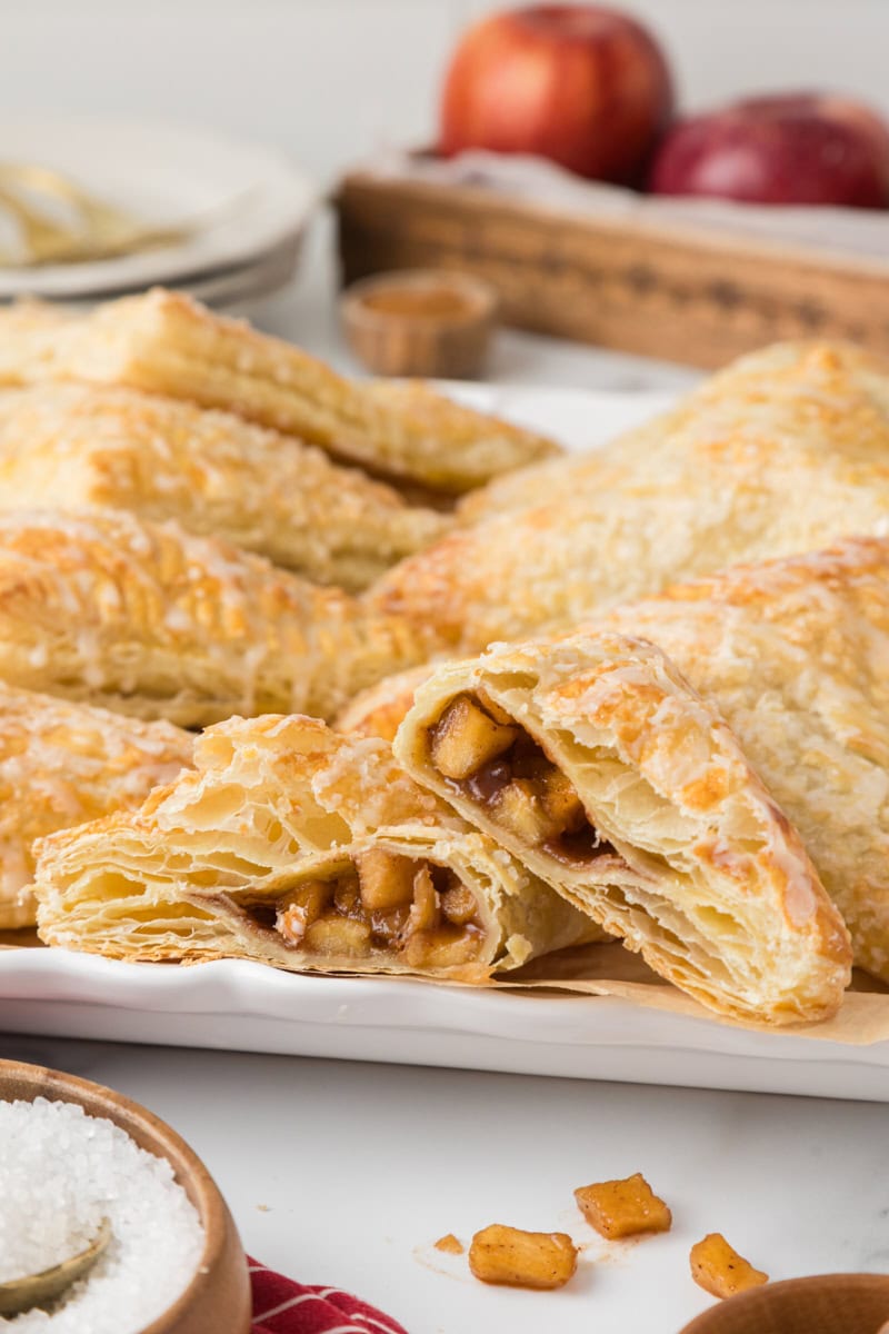 several apple turnovers on a white plate with the front turnover cut in half to show the filling