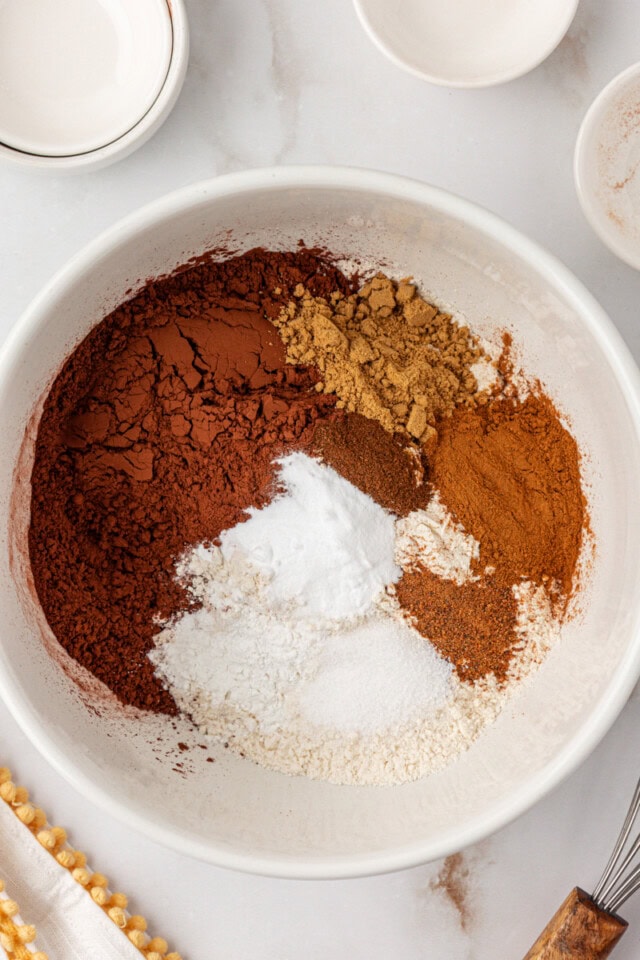 overhead view of flour, cocoa powder, baking soda, baking powder, salt, and spices in a white mixing bowl