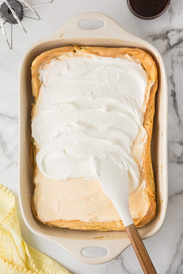 overhead view of whipped cream being spread over cream puff cake