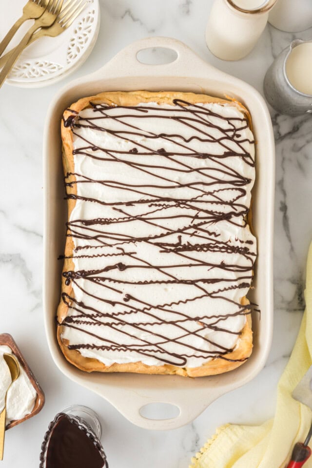 overhead view of cream puff cake topped with whipped cream and a drizzle of chocolate sauce in a white rectangular pan