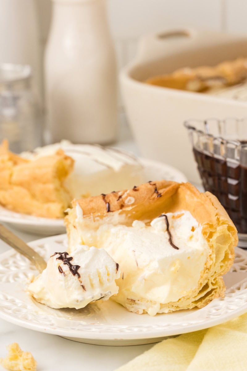 a slice of cream puff cake on a white plate with a bite on a fork