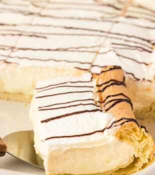 a slice of cream puff cake on a cake server resting inside the pan with the remaining cake