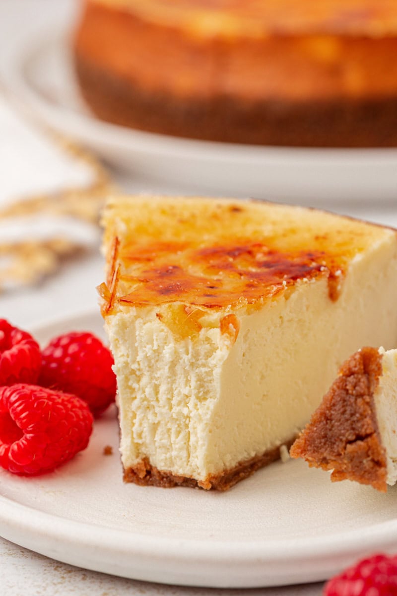 a slice of crème brûlée cheesecake on a plate with fresh raspberries and a bite on a fork