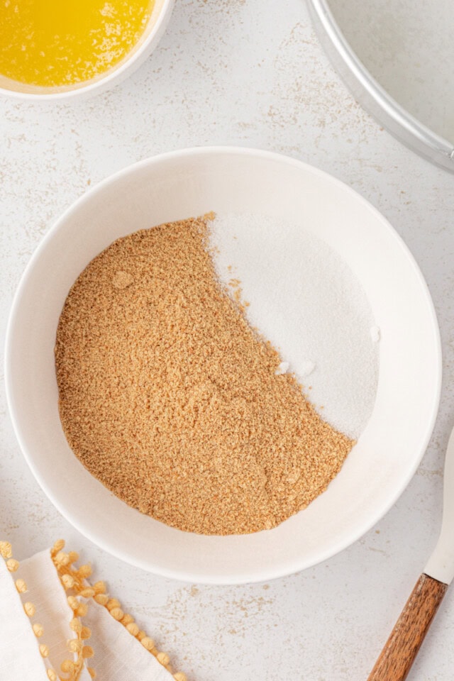 overhead view of graham cracker crumbs and sugar in a white mixing bowl