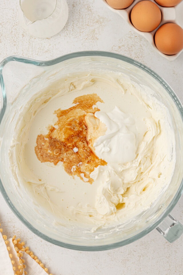 overhead view of cream, sour cream, vanilla, and salt added to beaten cream cheese and sugar