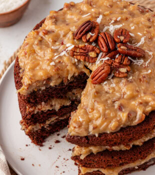 German chocolate cake on a white plate with a slice removed to show the layers of cake and frosting